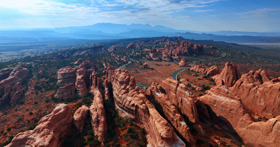 Unreal wall-shaped rounded rocks in the Arches National Park in Utah, USA. Approaching the highway loop with multiple cars parked. Aerial perspective.