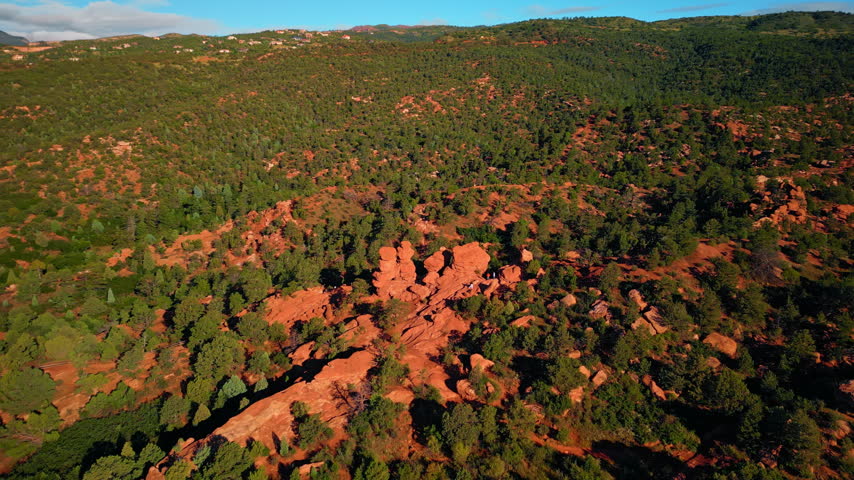 Flight high over the red rocky landscape with whimsical shapes of rocks. Two people take pictures standing on the boulders. Garden of the Gods Park, Colorado Springs, Colorado, USA.