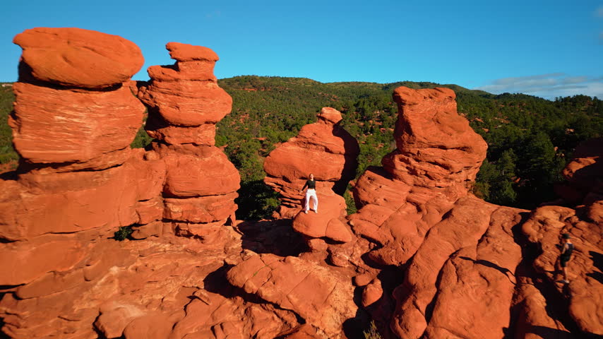 Flagstaff, USA, 24 August 2025: Distancing from the group of red rocks with a girl posing on them. Drone flight over the stunning territory of Garden of the Gods Park, Colorado Springs, Colorado, USA.