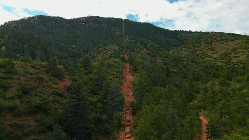 Flying above the steps leading to the top of the green mountain. Famous touristic attraction of the Manitou Springs Incline in Colorado, USA from drone.