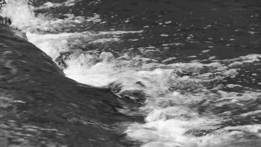 Black and white close up of rushing water flowing over a small weir