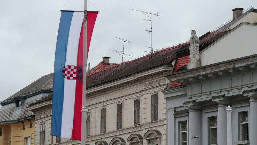 Croatian flag waving in the wind in front of some important looking buildings. Gloomy, somber lighting and grey skies.