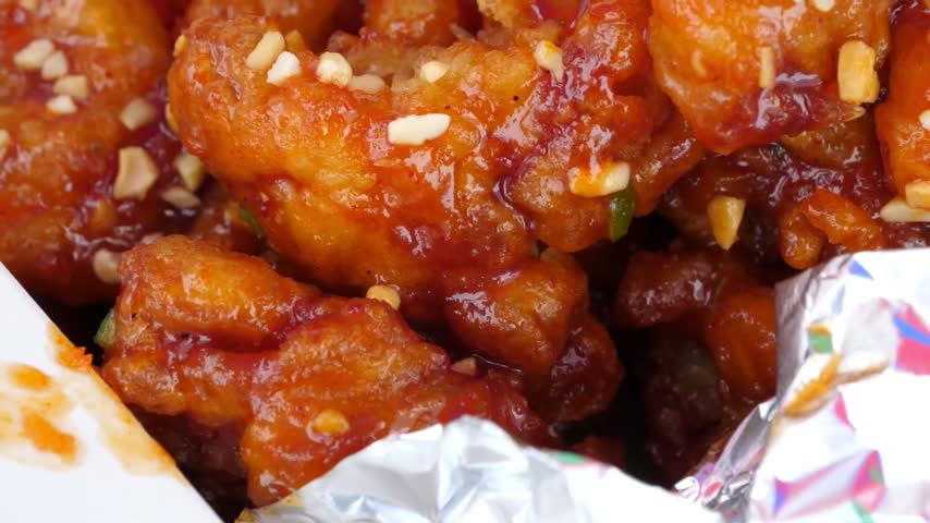 An appetizing, extreme close-up shot of crispy, golden-brown Korean fried chicken (Dakgangjeong) tossed in a glossy, sticky, vibrant red sweet and spicy glaze.