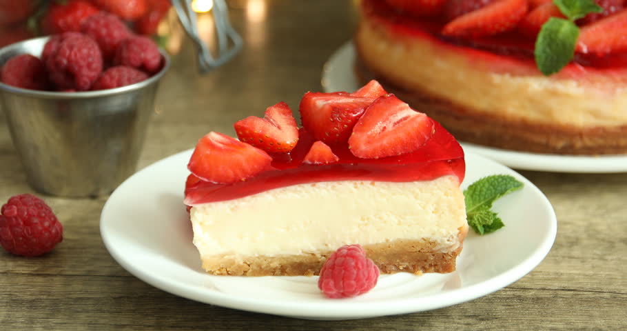 Woman putting mint onto piece of delicious cheesecake with strawberry jelly and fresh berries at wooden table, closeup