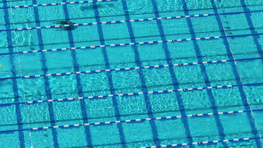 Overhead aerial view of outdoor swimming pool with multiple lanes where people swim laps in parallel motion across turquoise water.