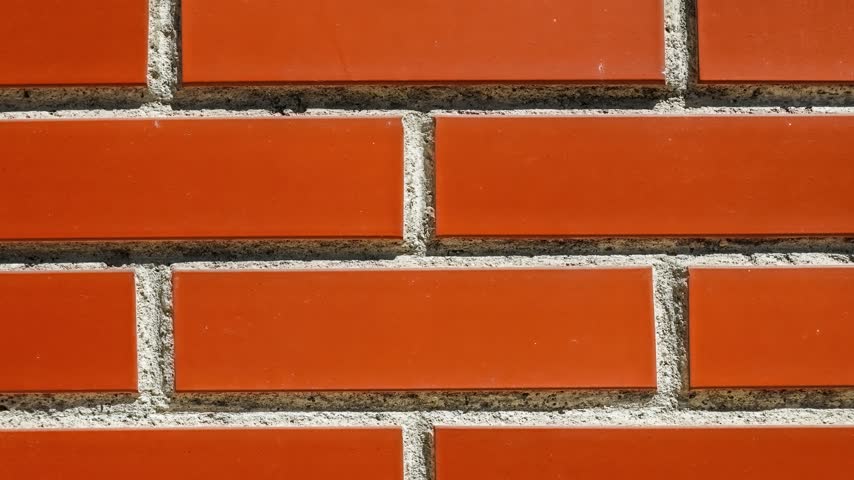 Seamless rotating loop of a glossy orange ceramic brick wall texture with textured cement mortar lines and clean modern tile patterns.