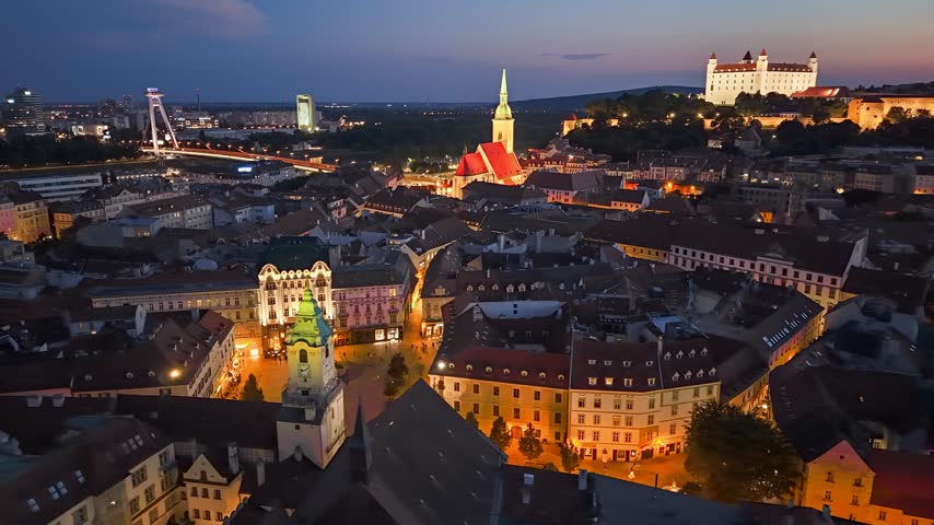 Evening aerial view captures historical buildings of Bratislava city illuminated at sunset. The iconic Bratislava castle stands high above the illuminated old town roofs, Slovakia