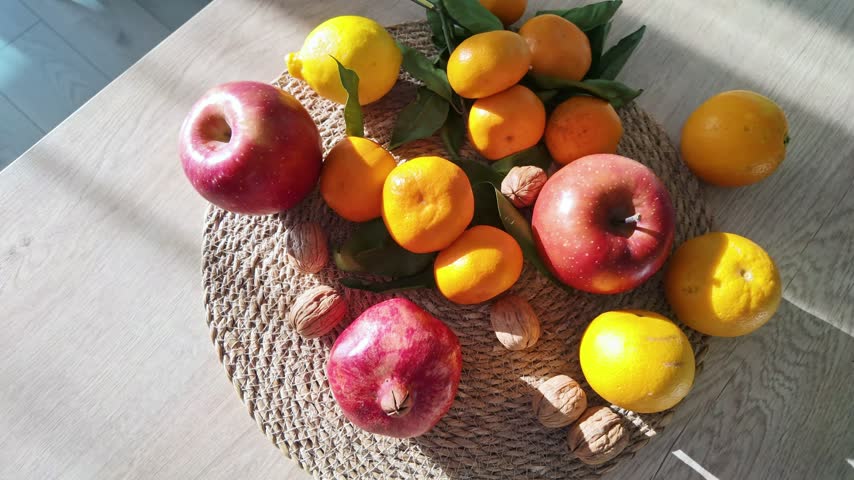 Assorted fresh apples, pomegranate, citrus fruits and walnuts arranged on a woven wicker tray.