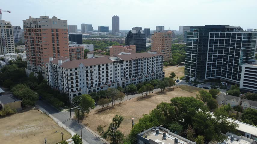 Expansive dry turf lot borders multi story apartment properties near Welborn Street, Dallas. Distant highrise towers rise above lush neighborhood greenery, DFW Metropolitan Area, Texas. USA