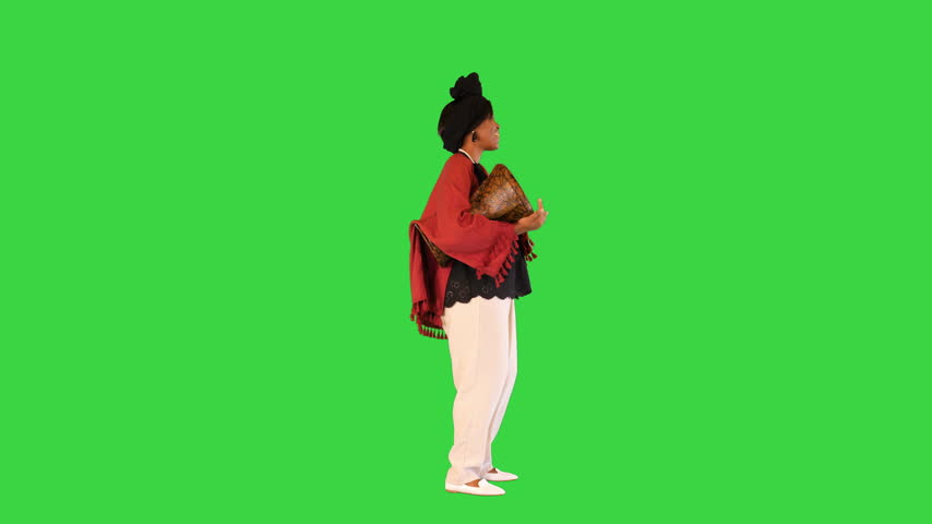 Cheerful african american woman in traditional clothes beats djembe drum and dances on a Green Screen, Chroma Key.