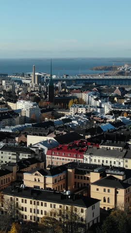 Aerial perspective over the kallio district in helsinki, finland, revealing historic architecture, the distinctive church steeple, and the expansive baltic sea under a bright blue sky