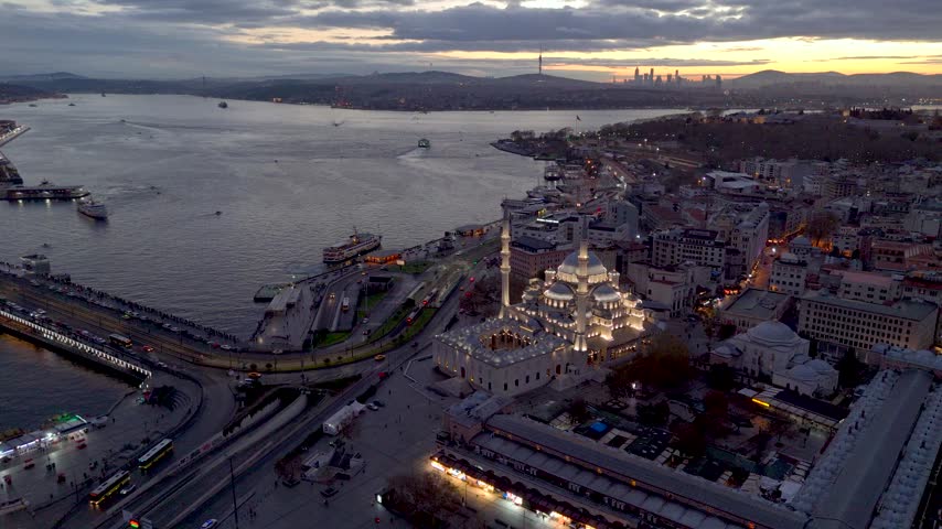 Aerial view of Istanbul at sunset, featuring the Bosphorus, a grand mosque, ferries, waterfront roads, historic buildings, and the city skyline glowing under a dramatic evening sky over Istanbul.