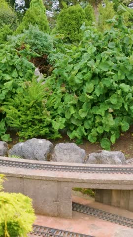 Model train hauling toy dinosaurs runs along miniature railway in Godshill model village, Isle of Wight, UK. Detailed garden layout, scale scenery and tourist attraction theme. Vertical format.