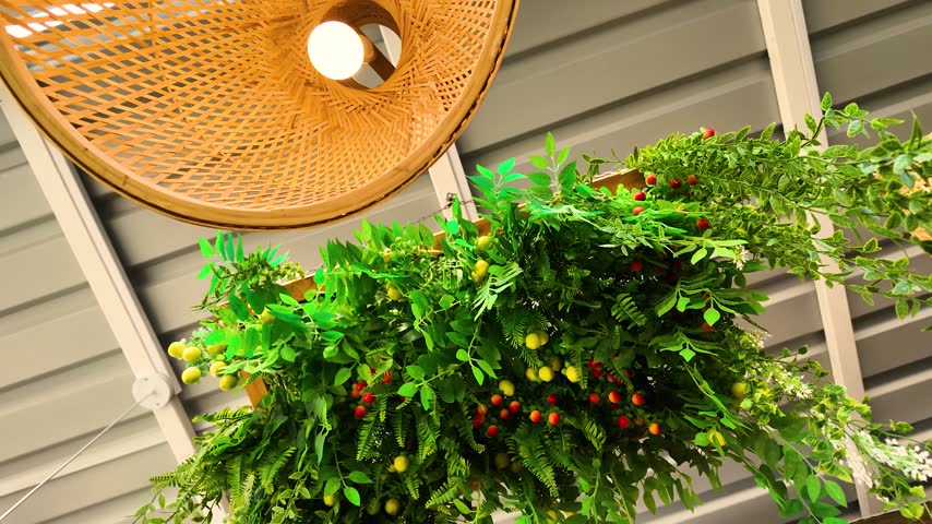 Boho-style hanging woven bamboo lamp shade and a planter with artificial greenery and berries on a patio ceiling