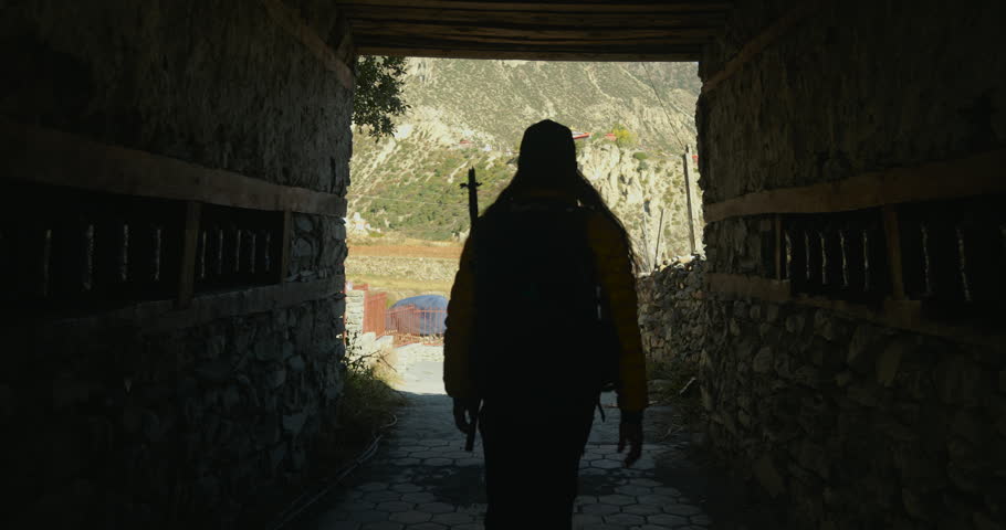 Annapurna Circuit, Manang Nepal, a solo male trekker with a backpack walking along a stone wall path toward mountain landscapes.