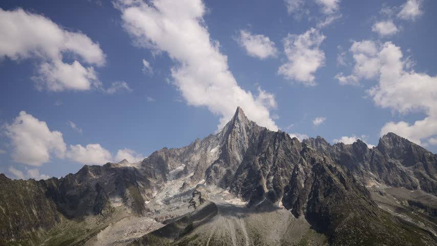 Timelapse of mountains and rapidly moving clouds along the Tour du Mont Blanc, capturing the changing atmosphere of one of the most spectacular trekking regions in the European Alps. Dramatic peaks, alpine ridges, deep valleys, glaciers, and open mountain slopes appear and disappear as clouds drift across the landscape. The accelerated movement of mist, fog, and changing weather creates a dynamic contrast with the rugged terrain, revealing the constantly evolving character of the high alpine environment. Sunlight breaking through the cloud cover can illuminate individual slopes and distant summits, creating shifting patterns of light and shadow across the scenery. The Tour du Mont Blanc passes through France, Italy, and Switzerland, offering exceptional views of the Mont Blanc massif and surrounding mountain ranges. This footage captures the natural beauty, powerful weather, and sense of wilderness associated with this iconic long distance hiking route, making it suitable for travel, adventure, nature, weather, outdoor recreation, and landscape content.