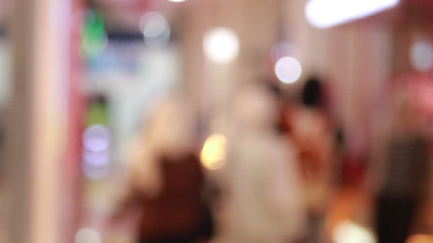 blured anonymous people walking through a crowded shopping mall corridor with bright lights and storefronts.