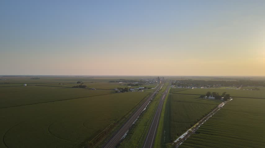 Aerial view at sunset of a highway and railroad leading toward a small town in rural Nebraska, USA