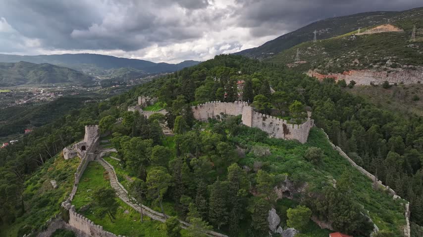 High-altitude drone shot pulling back to reveal the impressive Venetian castle walls of Nafpaktos built on a pine covered hill under a cloudy sky in Lepanto, Aetolia-Acarnania, Greece.