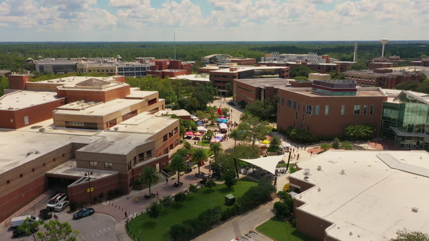 Drone shot of a vibrant student event at UCF in Orlando, capturing colorful tents, courtyards, and modern academic buildings across the busy university campus.