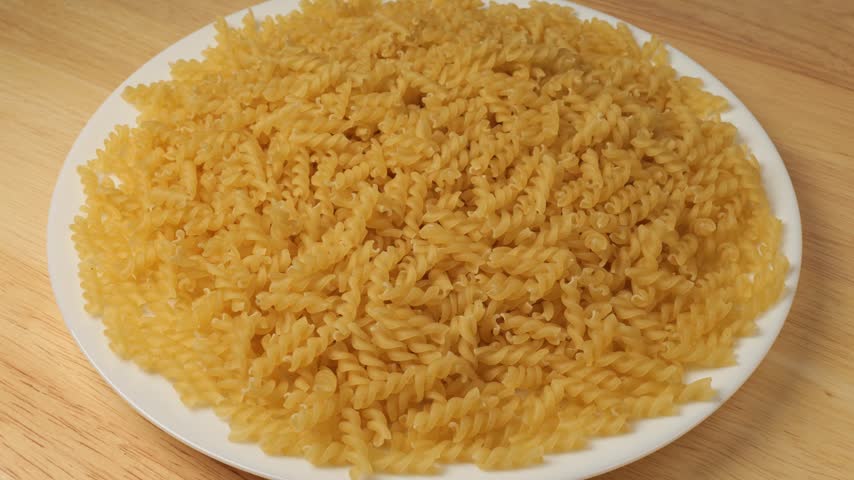 Uncooked fusilli pasta rotating on a plate