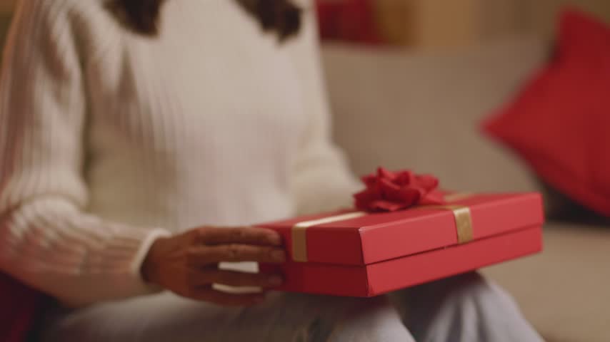 Closeup of young woman opening red Christmas gift box at home, 4K