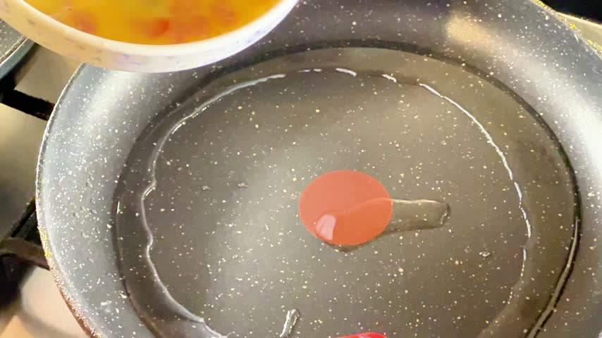 Close-up shot of raw beaten eggs mixed with diced ham and tomatoes pouring from a bowl into a hot frying pan. Ideal for breakfast commercials, cooking tutorials, and food ads.