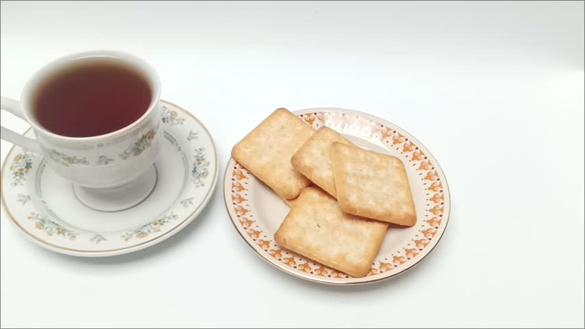 Person hand picking up crispy square biscuit from plate served with hot black coffee isolated on white background.