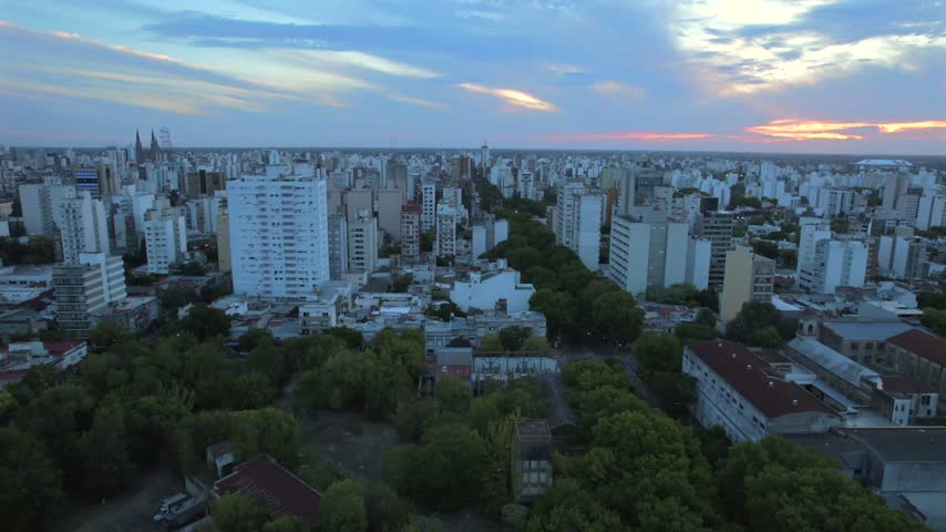 4K drone aerial view of La Plata, Buenos Aires, Argentina at sunset. Urban skyline, buildings and streets illuminated by warm evening light across the city.