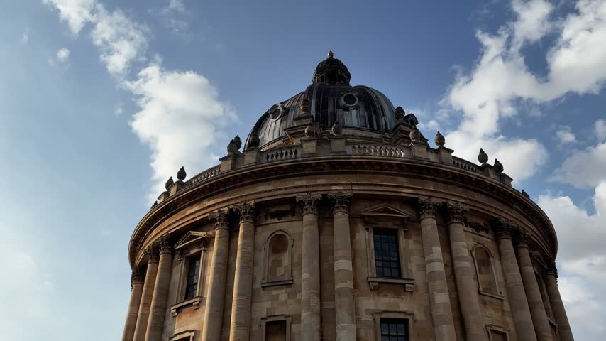 Famous Radcliffe Camera and historic architecture of Oxford University campus against cloudy blue sky, United Kingdom landmark.
