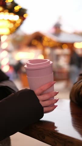 Girl Holds Cups Of Hot Mulled Wine At A Christmas Market Against Garland Lights, Vertical Video