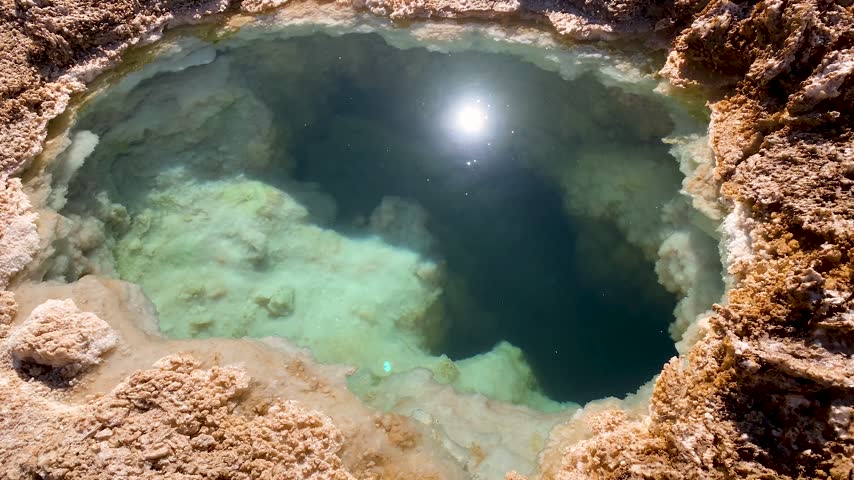 Salty water flowing slowly within ojos del salar lagoon in the atacama desert, a small but deep body of water surrounded by salt crust with the bright sun reflecting on the surface