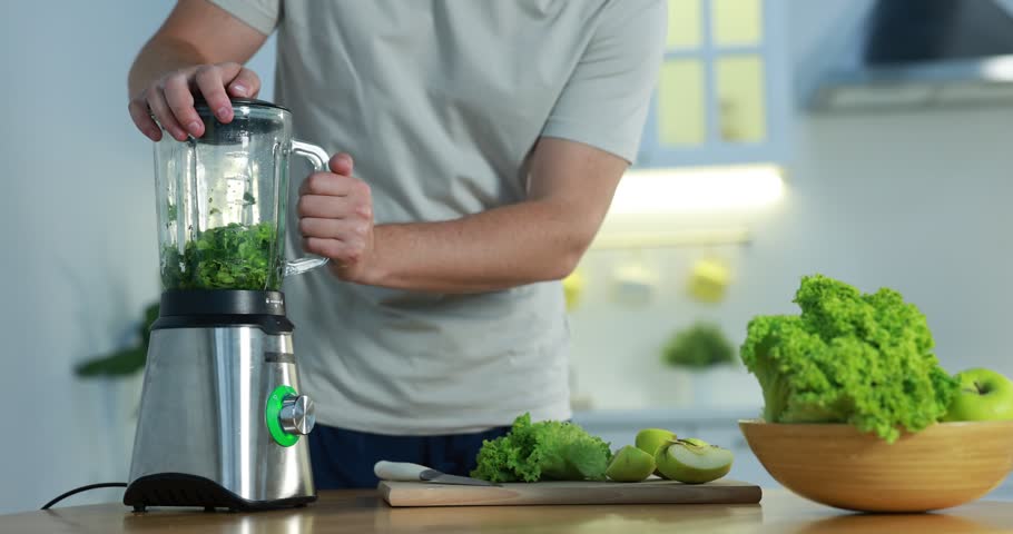Man making tasty green smoothie in blender at wooden table indoors, closeup