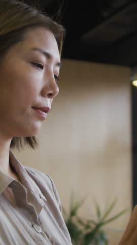 Animation of white triangles moving over asian businesswoman using digital tablet in office. Digital composite, multiple exposure, entrepreneur, art, business, design and technology concept.