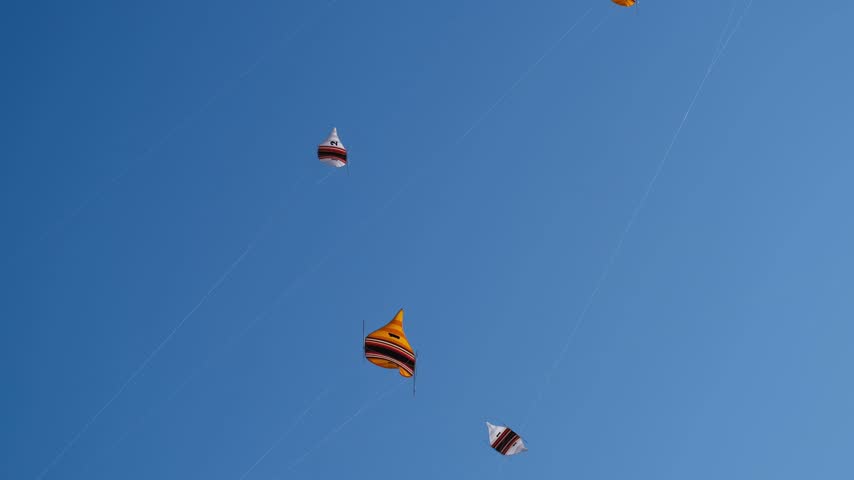 Many Colorful Kites Flying in a Blue Sky on Taut Strings Shimmering in Sunlight During an Annual Kite Festival, 4K 50fps