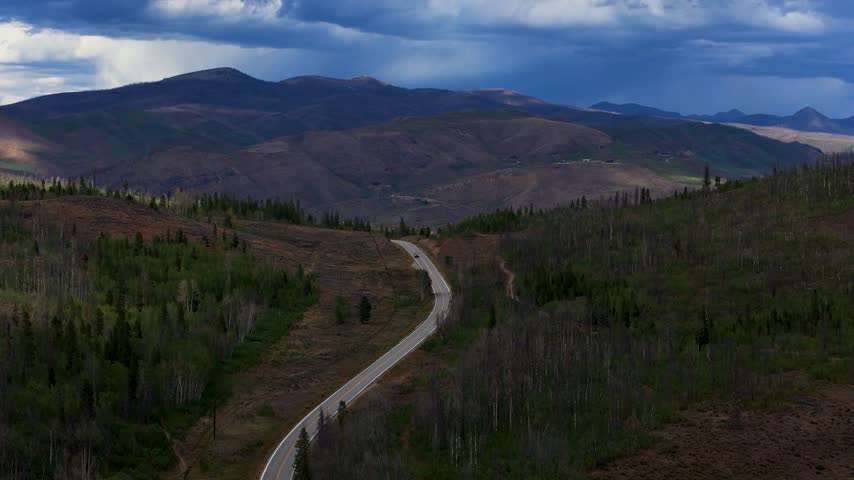 Aerial view of a winding road through a forested mountain landscape under a dramatic cloudy sky in Granby, Colorado, United States.