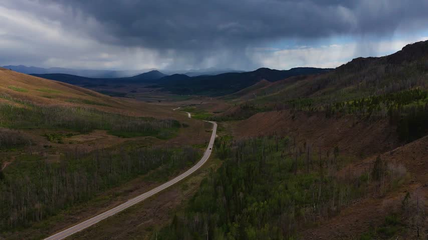 Aerial view of a winding road through a mountain valley under a dramatic stormy sky in Granby, Colorado, United States.