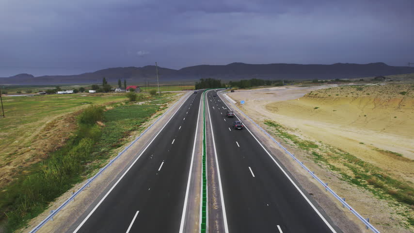 Drone footage nearly empty highway leading toward a dark cloud bank as the centered drone flight follows the quiet roadway recording road layout terrain depth and Dagestan scenery