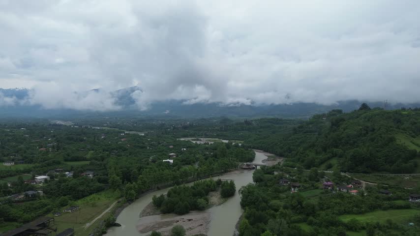 Aerial drone footage flying upstream along the Tekhuri mountain river and over Martvili village in Western Georgia. Overcast morning sky with dark grey clouds shortly after rain. Original, unedited 4K footage. 
