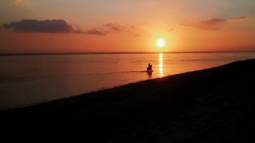 View of a silhouette of a person riding a horse in the ocean during a vibrant sunset at ARYA Sumba in Kodi, East Nusa Tenggara, Indonesia.