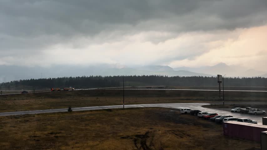 Distant freight train moves through rural Alberta under dramatic cloudy skies