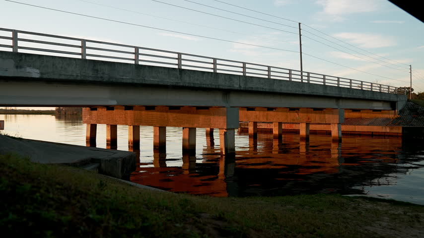 Concrete bridge stretching over the calm waters of Lake Minneola in Clermont, Florida, glowing warm orange in the light of a Florida sunrise.