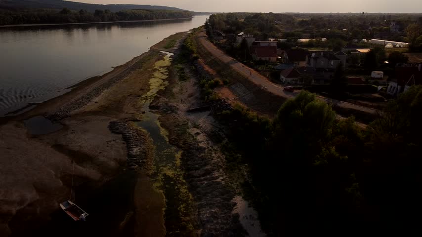 Danube River runs beside exposed sandbanks and riverside settlement at dusk, aerial medium pullback