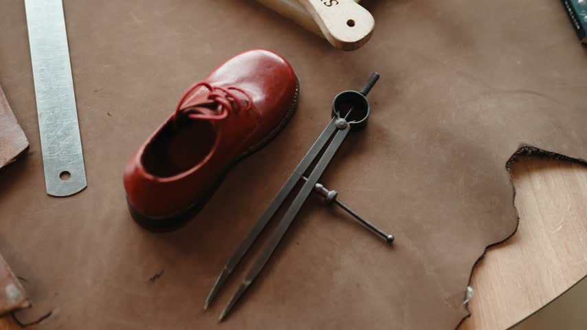 Red Child Shoe with Laces beside Steel Dividers and Ruler on a Brown Pattern Board