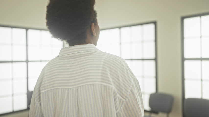 Woman holding documents leans forward on chair with hand on knee, preparing to sit and check papers in a sunlit building; anxiety anticipation.