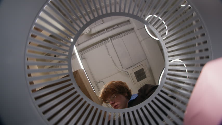 Young adult Caucasian man with glasses throwing paper coffee cup into trash bin, filmed from low angle inside basket. Footage is perfect for office sustainability and waste recycling campaigns