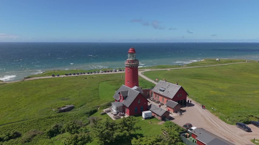Aerial drone footage circling Bovbjerg Lighthouse, showcasing vibrant green fields, dramatic coastline, and the powerful waves of the North Sea in Western Jutland, Denmark.
