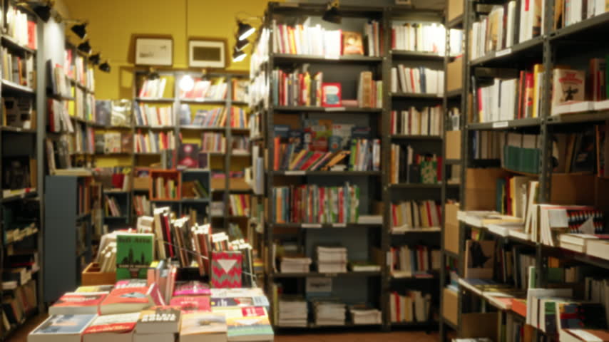 Bookstore interior with soft bokeh and defocused shelves and stacks of books, warm shop interior; background backdrop copyspace calm.