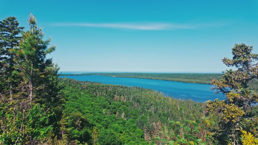 A bright blue lake surrounded by wild green forest on a sunny day and bright day from an up high overlook.
