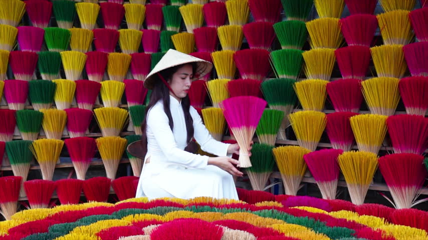 A young Vietnamese woman in a white national costume arranges colorful incense sticks in Hue, Vietnam.